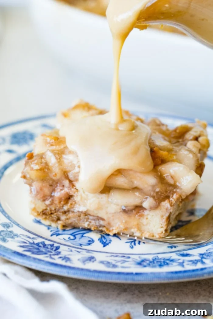 Warm Apple Pie Bread Pudding Drizzled with Vanilla Sauce 5 a large slice of apple pie bread pudding with vanilla sauce sitting on a blue china plate with a bite taken out of the front.