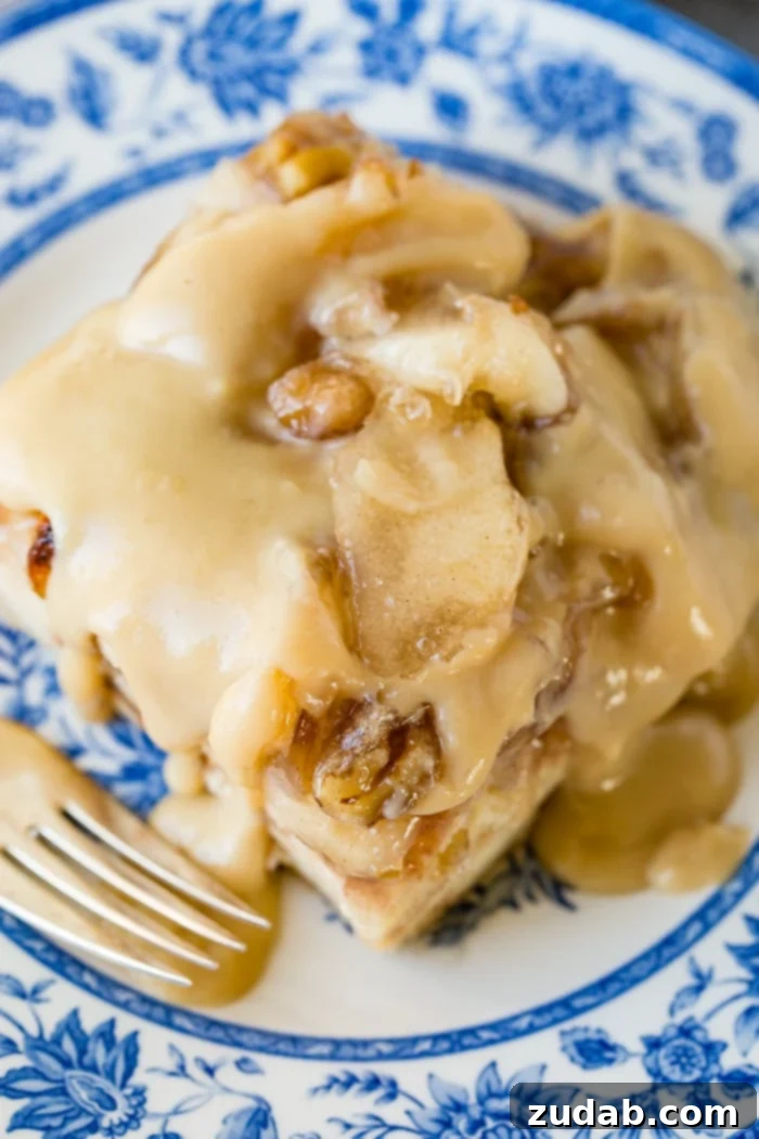 Warm Apple Pie Bread Pudding Drizzled with Vanilla Sauce 6 a large slice of apple pie bread pudding with vanilla sauce sitting on a blue china plate with a bite taken out of the front.