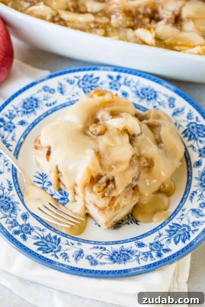 Warm Apple Pie Bread Pudding Drizzled with Vanilla Sauce 8 a large slice of apple pie bread pudding with vanilla sauce sitting on a blue china plate with a bite taken out of the front.