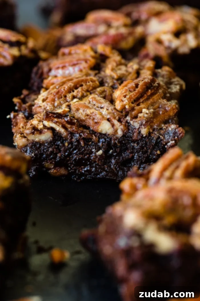 Close-up of three pecan pie brownies stacked, revealing the thick, glossy pecan topping and dense chocolate brownie.