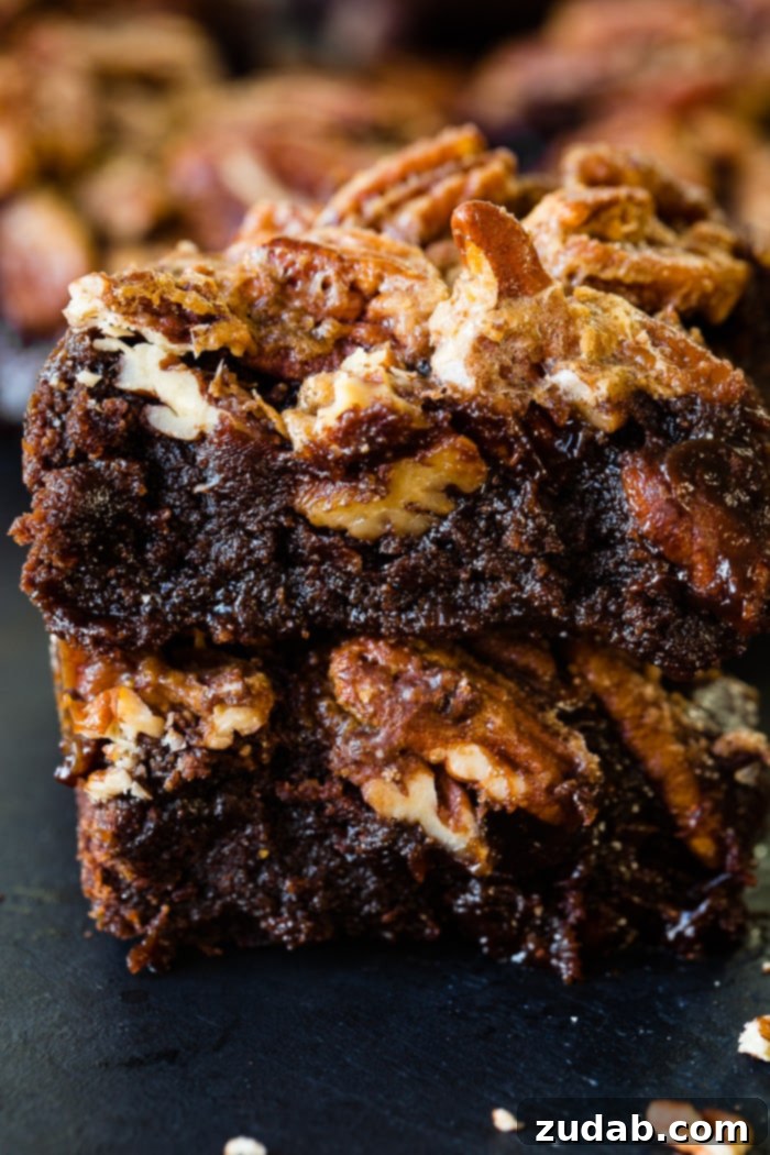 A stack of two pecan pie brownies on a cooling rack, with more brownies in the background, hinting at their fresh-baked goodness.