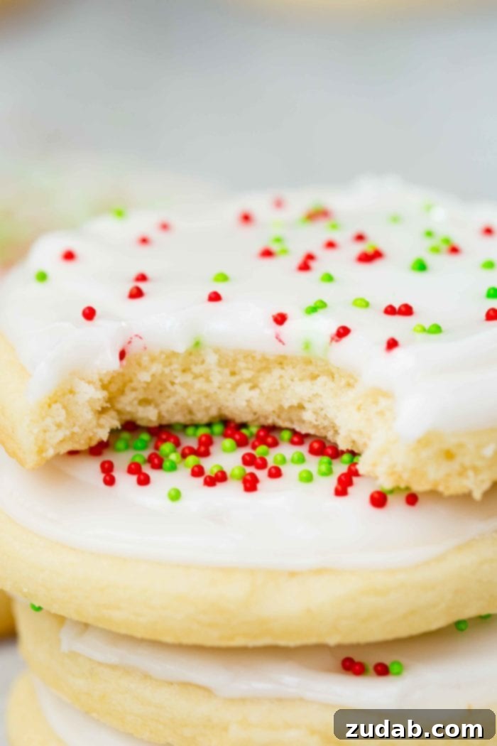 Festive Peppermint White Chocolate Sugar Cookies 6 a closeup photo of a stack of sugar cookies with white frosting and red and green sprinkles with a bite out of the top cookie
