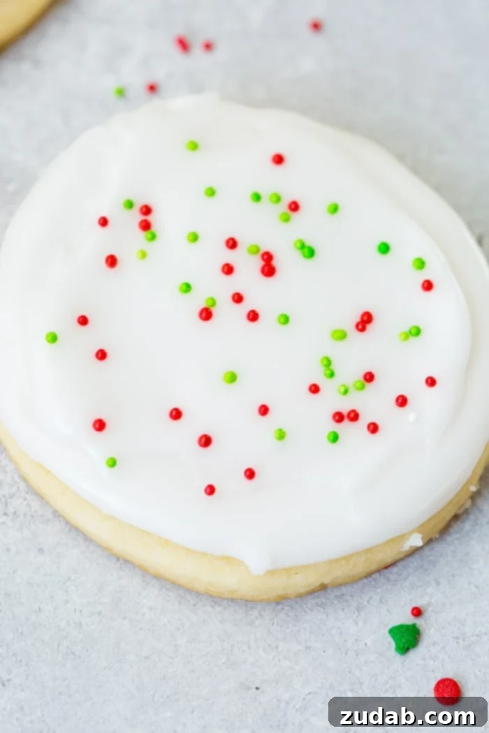 Festive Peppermint White Chocolate Sugar Cookies 7 A closeup photo of a sugar cookie frosted with white royal icing with red and green sprinkles