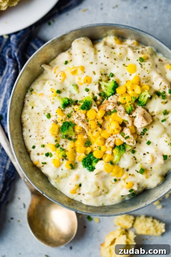 Hearty Chicken & Garden Chowder 3 A silver bowl brimming with Chicken Potato Broccoli Corn Chowder, accompanied by a gold spoon and a blue striped towel on a grey wooden background, highlighting the rich textures of the soup.