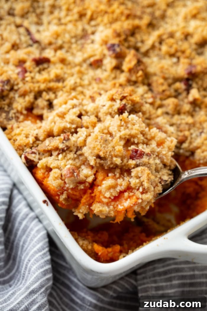 This Sweet Potato Souffle Outshines Ruths Chris 2 A glistening sweet potato souffle with a crunchy brown sugar pecan topping in a white casserole dish, with a silver spoon poised to serve.