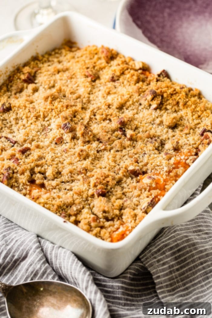 This Sweet Potato Souffle Outshines Ruths Chris 3 A close-up of a serving of fluffy sweet potato souffle with a golden brown sugar crust being scooped from a white baking dish.