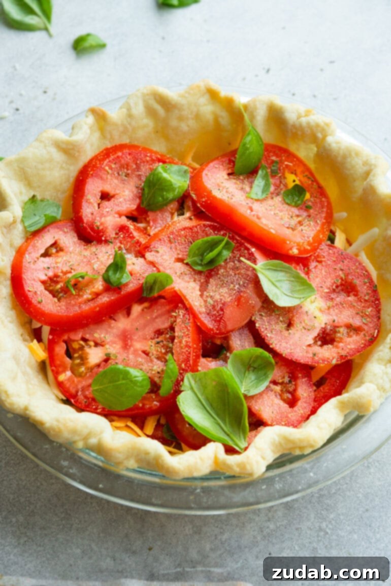 Southern Comfort in a Crust Tomato Pie 5 a photo of a partially baked pie crust filled with layers of sliced tomatoes, cheese and fresh basil leaves