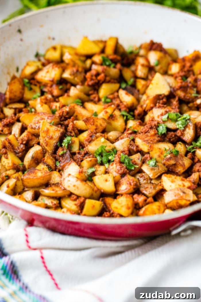 Simple Chorizo Potato Skillet 10 A red and white skillet filled with golden, crispy 3-ingredient chorizo potatoes, topped with fresh green cilantro, presented beautifully for a savory breakfast or side dish.