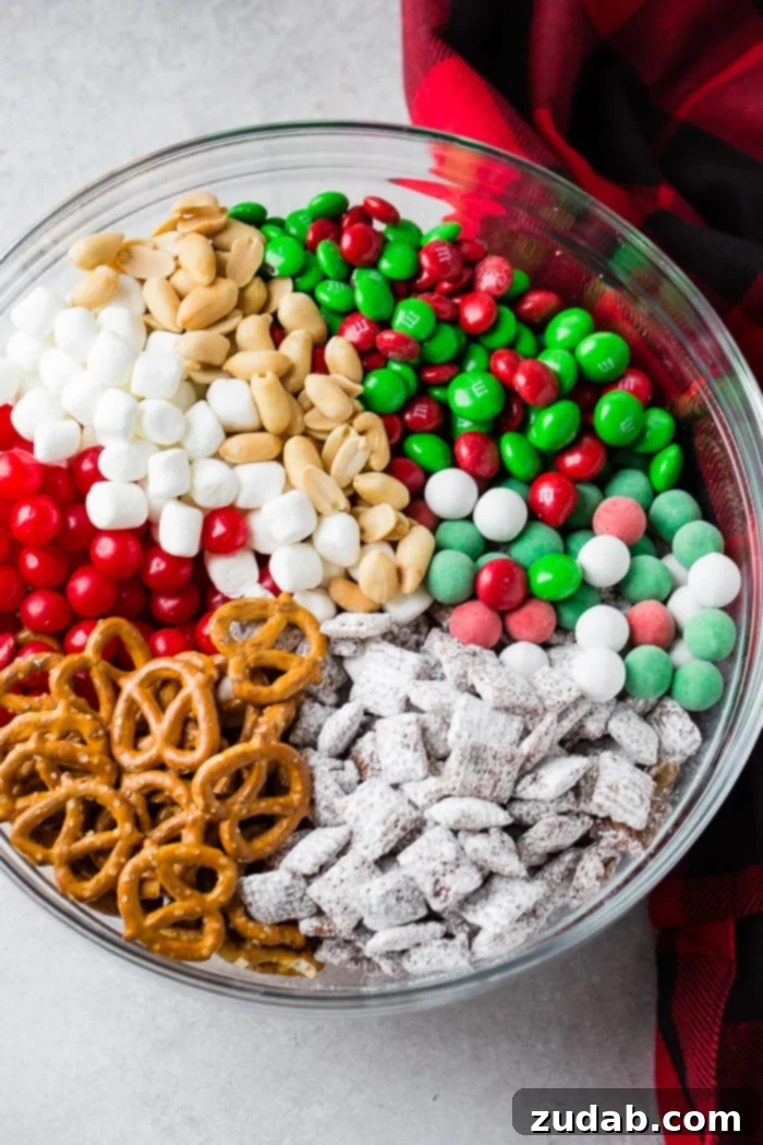Jolly 5 Minute Christmas Crunch 3 Close-up of a festive 5-Minute Christmas Snack Mix in a clear glass bowl, showcasing the variety of ingredients like M&Ms, pretzels, and candies.