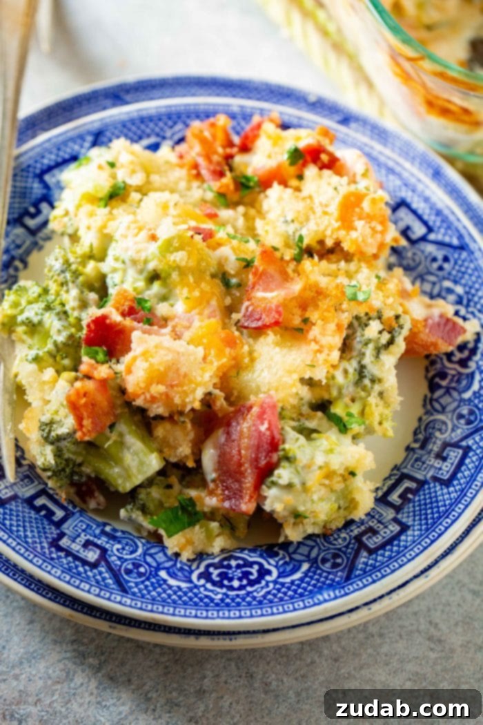 Ultimate Cheesy Bacon Broccoli Bake 4 A single serving of creamy cheesy broccoli casserole, topped with crispy bacon and panko bread crumbs, resting on a rustic blue plate.