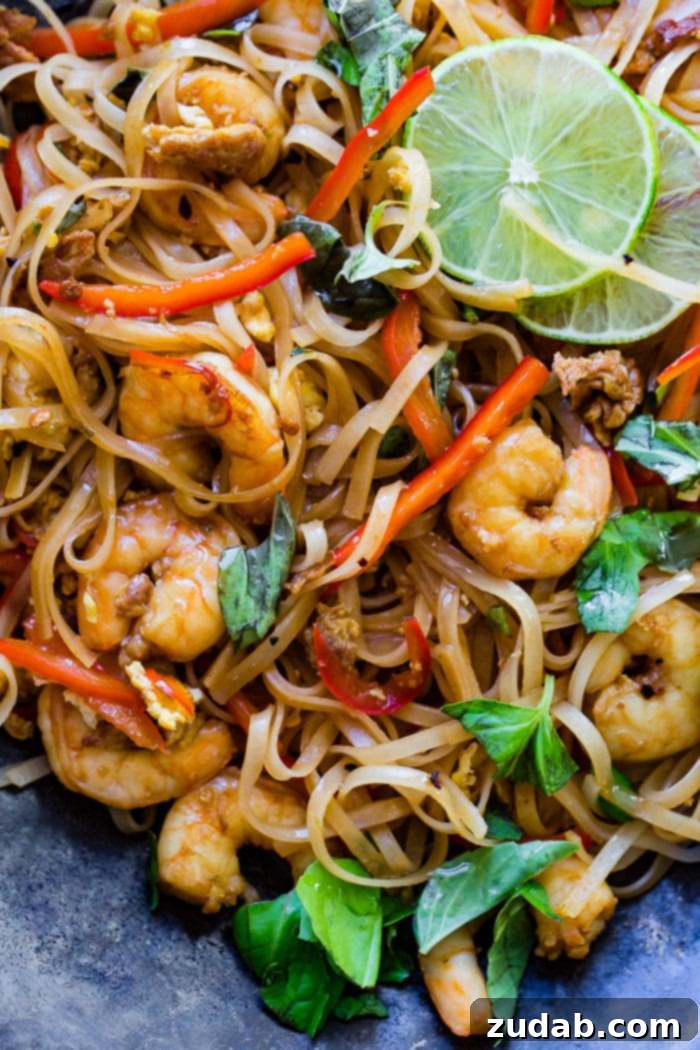 Zesty One-Pan Asian Shrimp Noodles 5 A delightful plate of One Pan Simple Asian Shrimp Noodles, showcasing shrimp, rice noodles, red bell peppers, and fresh basil, artfully garnished with lime slices.
