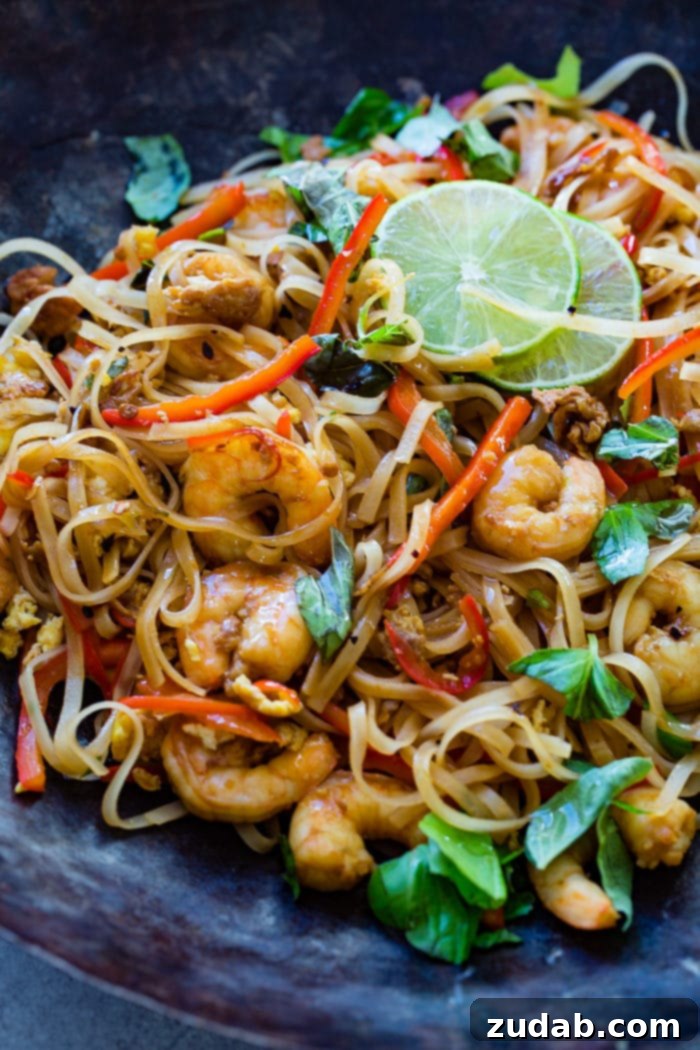Zesty One-Pan Asian Shrimp Noodles 6 A close-up of a blue plate filled with One Pan Simple Asian Shrimp Noodles, showcasing succulent shrimp, rice noodles, red bell peppers, and fresh basil, garnished with lime wedges.