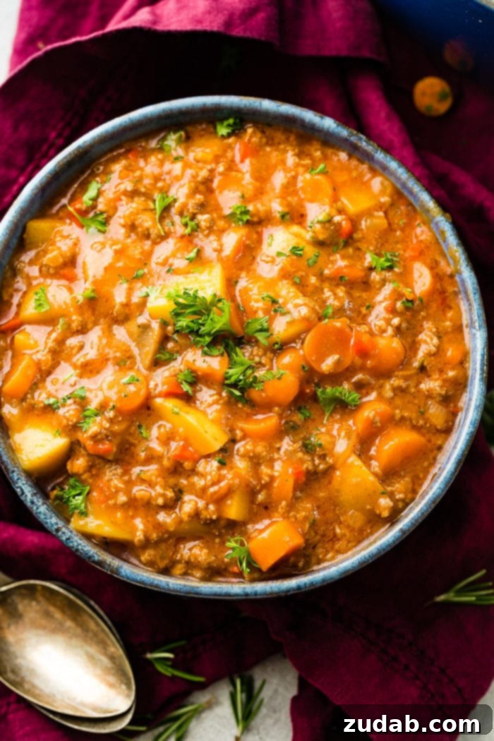 Hearty Weeknight Ground Beef Stew 2 a magenta napkin with two antique spoons next to a blue rimmed ceramic bowl full of quick and easy ground beef stew with carrots and potatoes