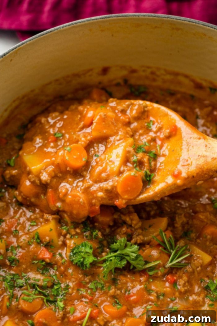 Hearty Weeknight Ground Beef Stew 7 a blue le creuset pot full of quick and easy ground beef stew with potatoes, carrots and parsley on top