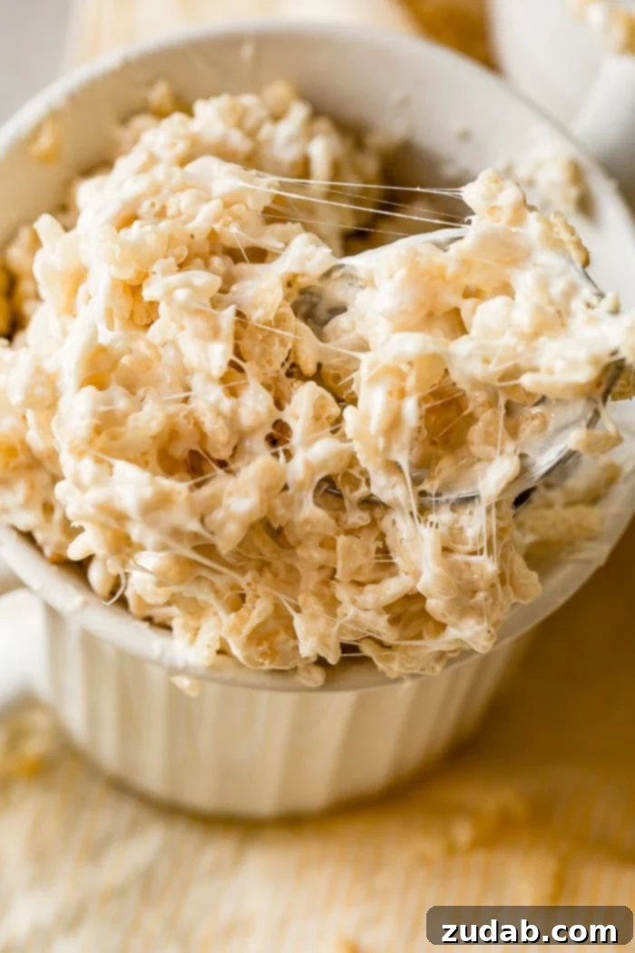 2-Minute Rice Krispie Treat in a Mug 2 A photo of gooey rice krispie treat in a white mug with someone taking a spoonful out.