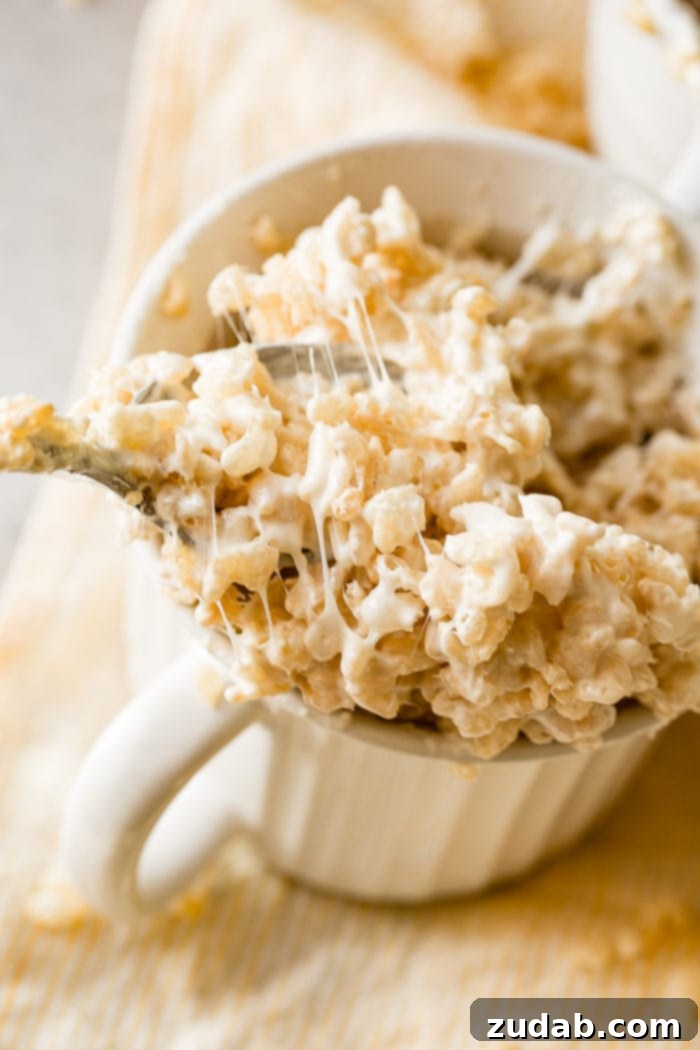 2-Minute Rice Krispie Treat in a Mug 5 A photo of a white mug full of gooey Rice Krispie treats with a spoonful being pulled out.