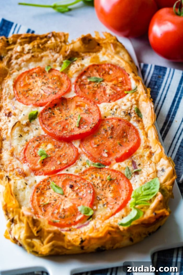 Country Tomato Galette 2 A freshly baked rustic tomato tart, generously topped with vibrant red tomato slices, creamy cheeses, and aromatic fresh basil leaves, resting on a serving platter.