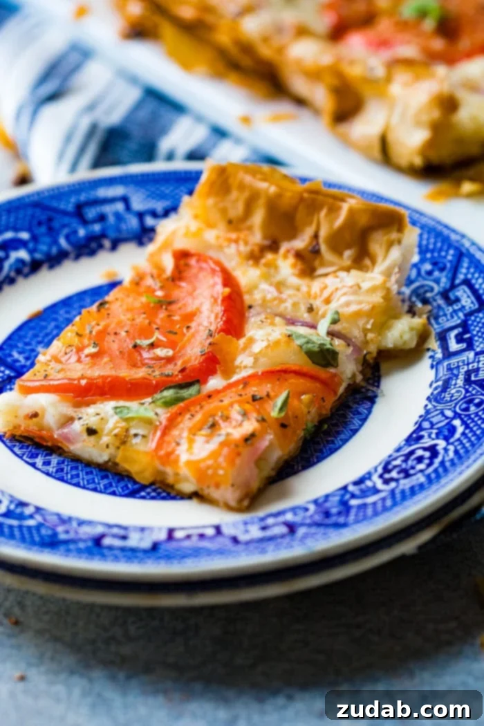 Country Tomato Galette 3 A single slice of rustic tomato tart, adorned with tomatoes, cheese, and fresh basil, artfully presented on a blue and white patterned plate, highlighting its delicious texture.