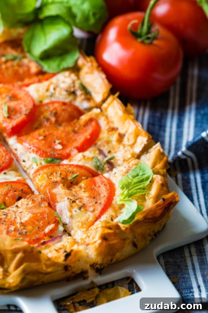 Country Tomato Galette 4 A beautifully sliced rustic tomato tart, showcasing its layers of golden filo, melted cheese, and fresh tomato, arranged on a pristine white cutting board, ready to serve.