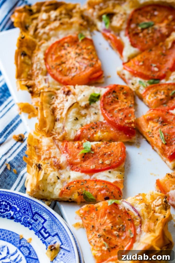 Country Tomato Galette 6 A close-up view of a sliced rustic tomato tart on a white cutting board, highlighting the rich melted cheeses and juicy tomato slices within its flaky crust.