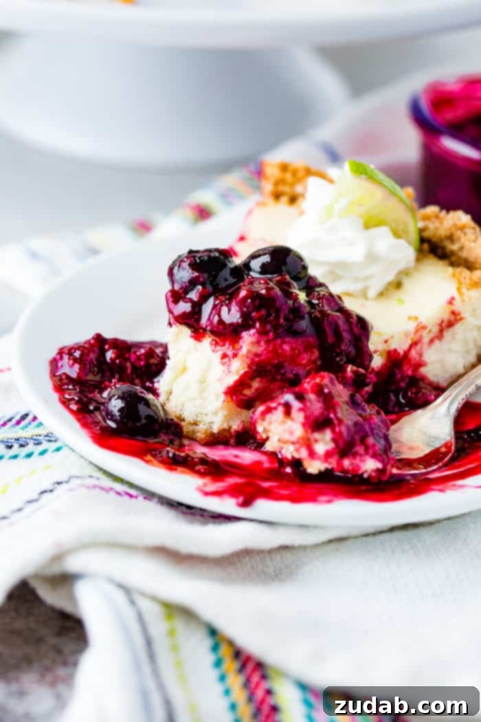 Sunshine Lime Cheesecake with Berry Swirl 12 A photo of a slice of lime cheesecake with triple berry sauce on a white plate with a bite taken out of it with berry sauce dripping all around it.