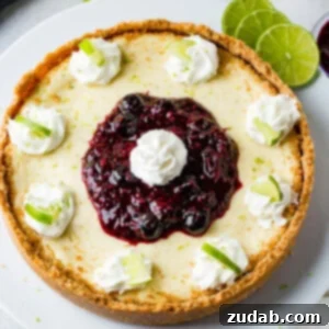 Sunshine Lime Cheesecake with Berry Swirl 13 An aerial photo of a whole cheesecake on a white serving platter with dollops of whipped cream around the edges with a slice of lime in each dollop and a pile of triple berry sauce in the middle with a dollop of whipped cream on top