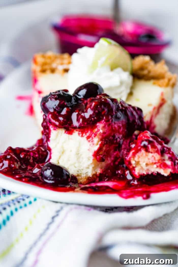 Sunshine Lime Cheesecake with Berry Swirl 4 A photo of a slice of lime cheesecake with triple berry sauce on a white plate with a bite taken out of it with berry sauce dripping all around it.