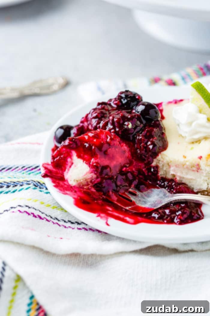 Sunshine Lime Cheesecake with Berry Swirl 6 A photo of a slice of lime cheesecake with triple berry sauce on a white plate with a bite being taken out with a fork with berry sauce dripping all around it.