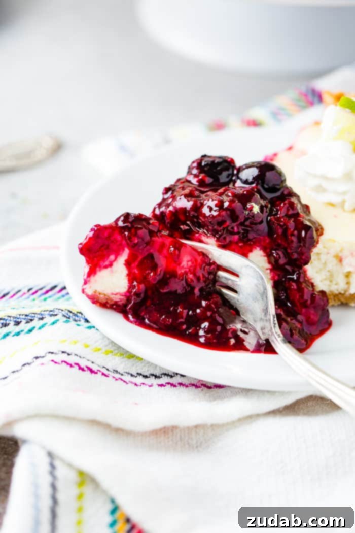 Sunshine Lime Cheesecake with Berry Swirl 8 A photo of a slice of lime cheesecake with triple berry sauce on a white plate being cut into with a fork with berry sauce dripping all around it.