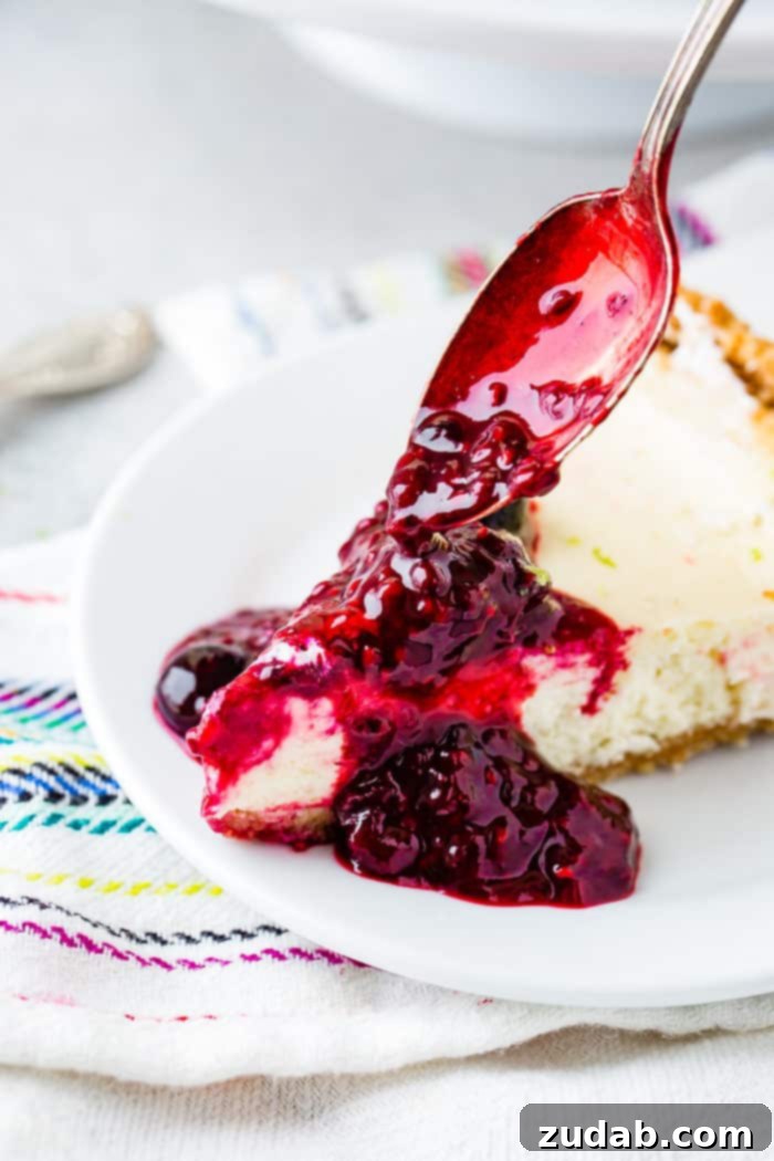 Sunshine Lime Cheesecake with Berry Swirl 10 A photo of triple berry sauce being poured with a spoon onto a slice of lime cheesecake.