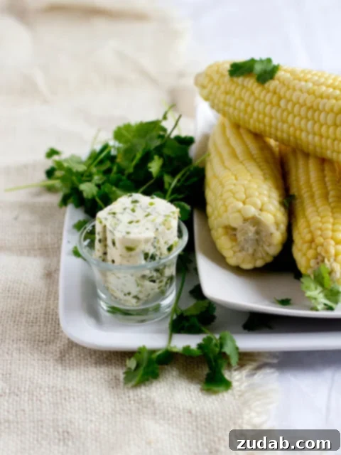 Cilantro Buttered Corn 2 Cilantro Butter Corn on the cob, garnished with fresh cilantro leaves, on a rustic wooden surface.