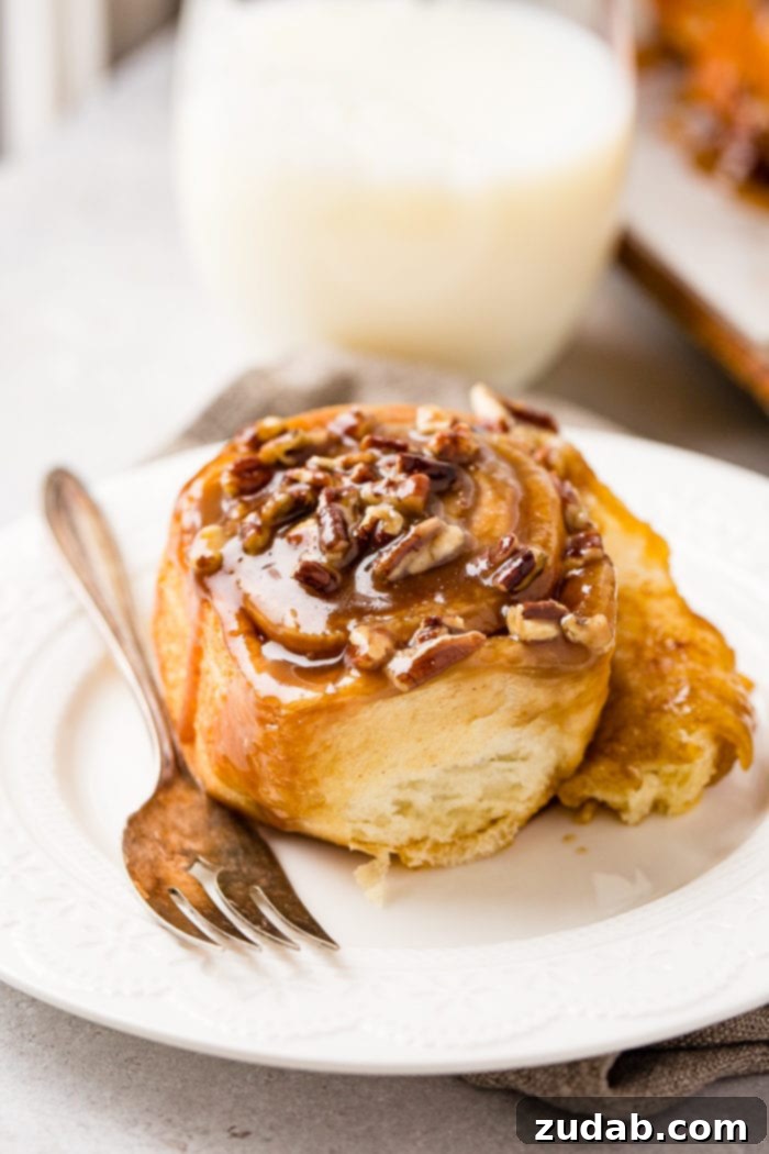 Irresistible Pecan Sticky Buns 5 A photo of a sticky bun sitting on a white plate with a fork next to it.
