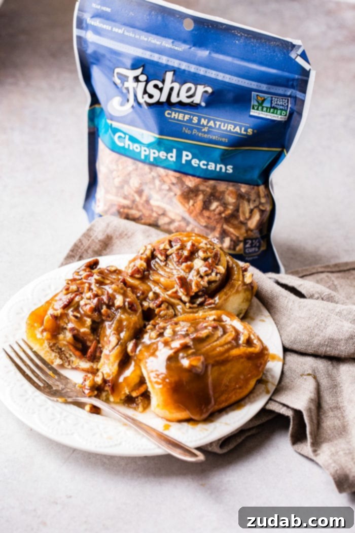 Irresistible Pecan Sticky Buns 8 A photo of three sticky buns on a white plate with a fork sitting next to them and a bag of Fisher chopped pecans in the background.