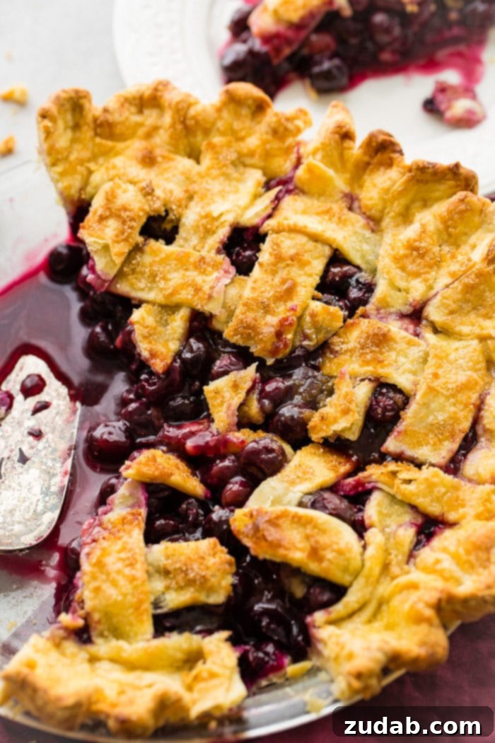 Effortless Blueberry Pie 4 A photo of a blueberry pie with a lattice top, with a few slices already removed and a pie server resting in the pan.