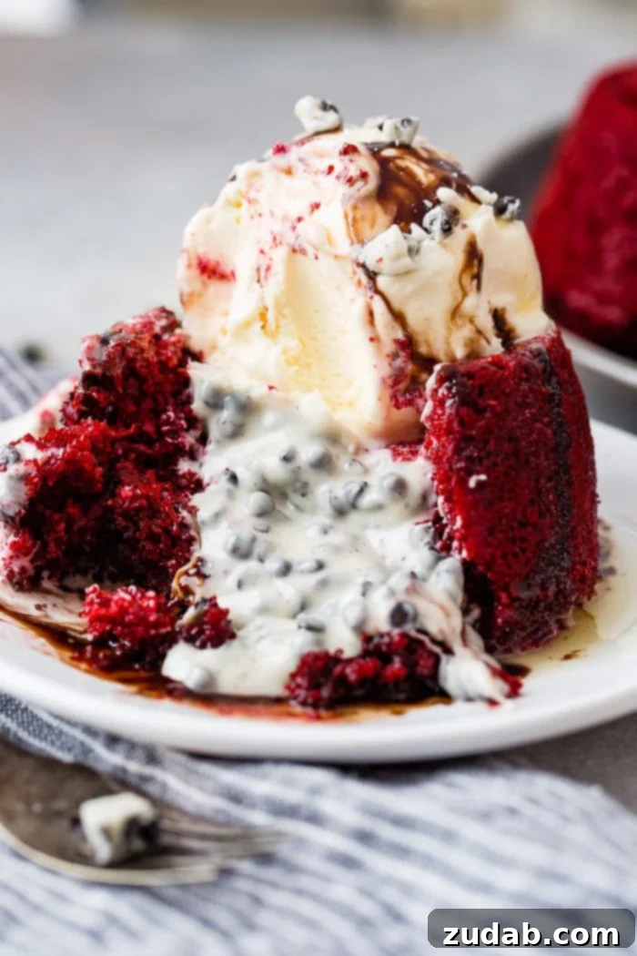 A photo of a vibrant red velvet molten lava cake filled with gooey cookies and cream chocolate, elegantly spilling out onto the plate. It's crowned with a generous scoop of creamy vanilla ice cream and drizzled with a rich chocolate sauce, highlighting its irresistible allure.