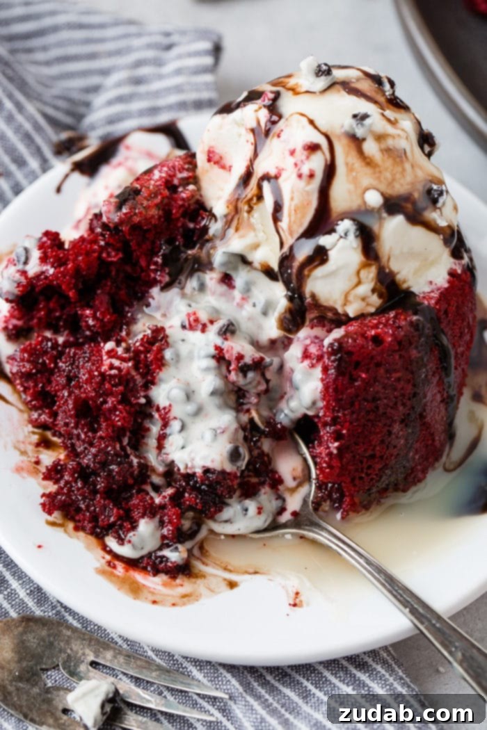 A delicious red velvet molten lava cake, cut open to reveal a rich, flowing cookies and cream filling that spills alluringly onto the plate. It's elegantly garnished with a scoop of creamy ice cream and a drizzle of decadent chocolate sauce, creating a perfect balance of flavors and textures.