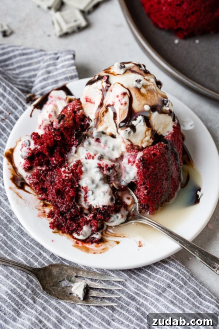 A red velvet molten lava cake, artfully sliced to expose a cascade of cookies and cream filling, beautifully spilled across the plate. The dessert is crowned with a scoop of rich ice cream and adorned with a generous drizzle of chocolate sauce, creating an irresistible visual and culinary experience.