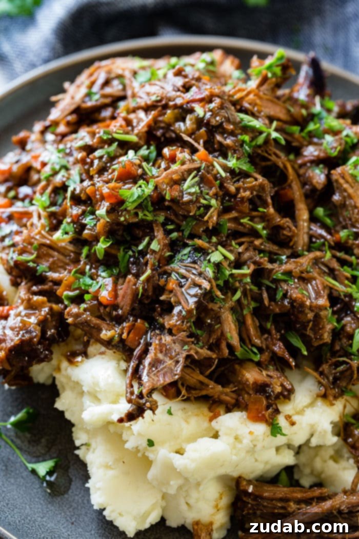 Hearty Oven-Braised Pot Roast 6 A close up photo of a pile of mashed potatoes on it covered in juicy shredded braised beef topped with chopped fresh parsley.