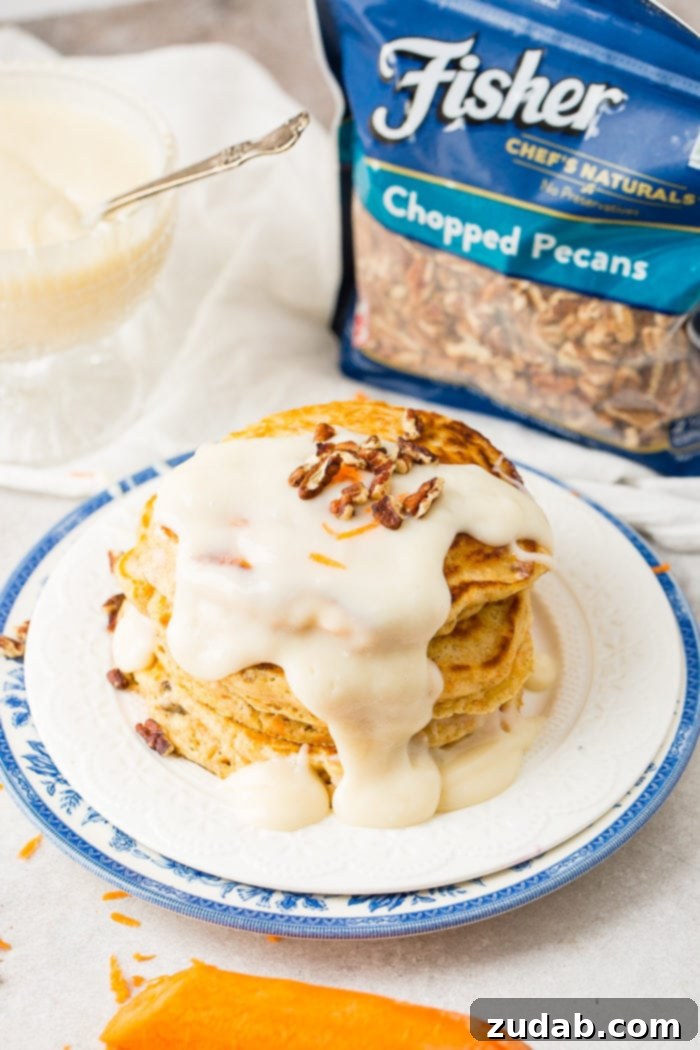 Sweet and Spiced Carrot Cake Pancakes 4 A photo of a stack of four carrot cake pancakes with a thick white cream cheese sauce poured over the top with a few chopped pecans and shredded carrots on top with a bag of Fisher chopped pecans in the background.