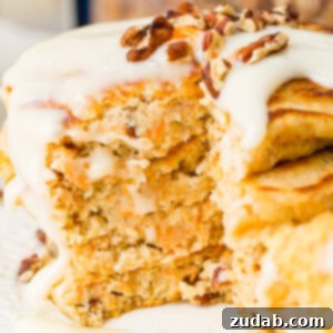 Sweet and Spiced Carrot Cake Pancakes 8 A photo of a stack of four carrot cake pancakes with a thick white cream cheese sauce poured over the top with a few chopped pecans and shredded carrots on top.