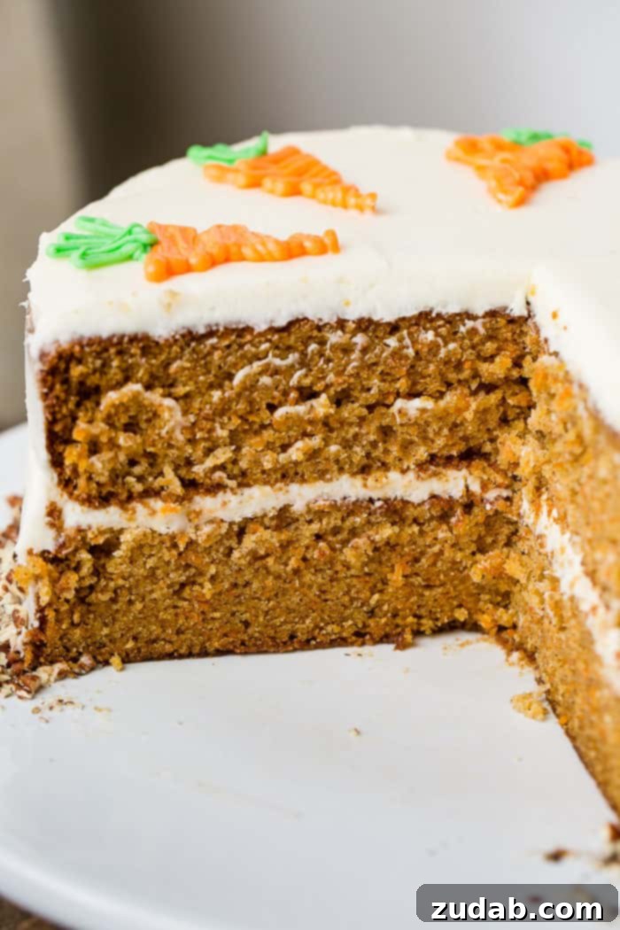 My Signature Spiced Carrot Cake 2 A beautifully frosted two-layer carrot cake on a white cake stand, with a slice removed, revealing moist interior and creamy white frosting between layers. The cake is adorned with delicate white chocolate decorative carrots.
