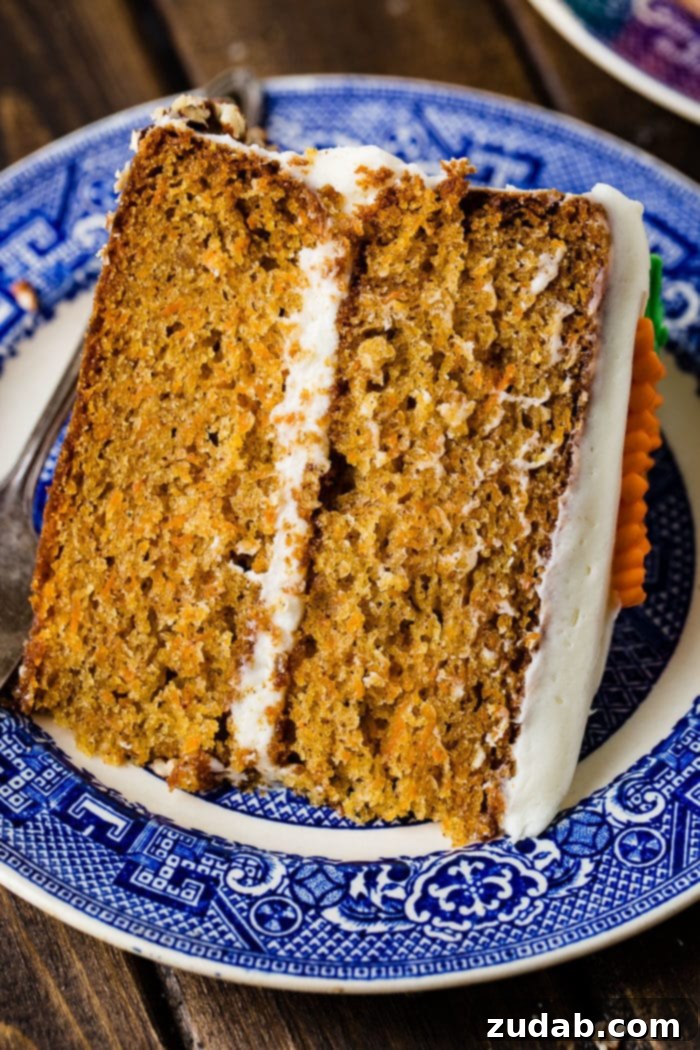 My Signature Spiced Carrot Cake 4 A tantalizing slice of two-layer carrot cake, featuring thick cream cheese frosting, resting on its side on an elegant blue and white plate.