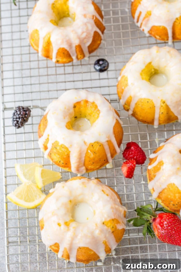 Zesty Lemon Poppy Seed Bundtlets 5 A photo of several mini lemon poppy seed bundt cakes on a silver wired cooling rack topped with a creamy white lemon glaze.