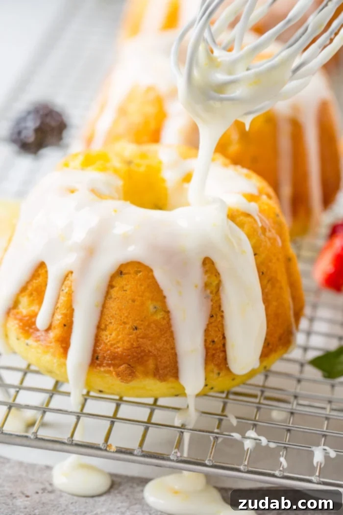 Zesty Lemon Poppy Seed Bundtlets 7 A photo of a mini lemon poppy seed bundt cakes on a silver wired cooling rack with a creamy white lemon glaze being poured on top.