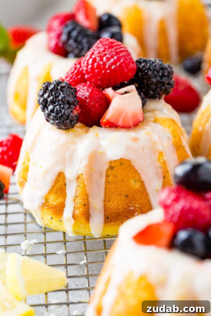 Zesty Lemon Poppy Seed Bundtlets 8 A photo of a mini lemon poppy seed bundt cakes on on a silver wire cooling rack with a lemon glaze on top and fresh berries.