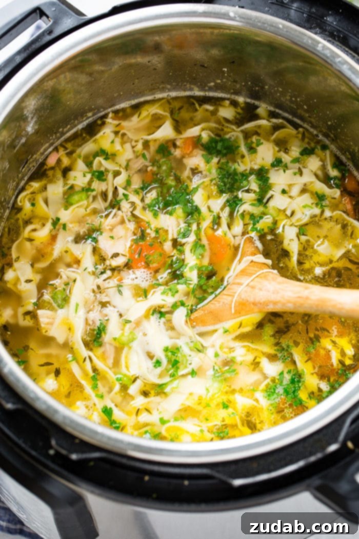 A wooden spoon stirring rich, golden chicken noodle soup directly in the Instant Pot, highlighting the ease and convenience of pressure cooking.