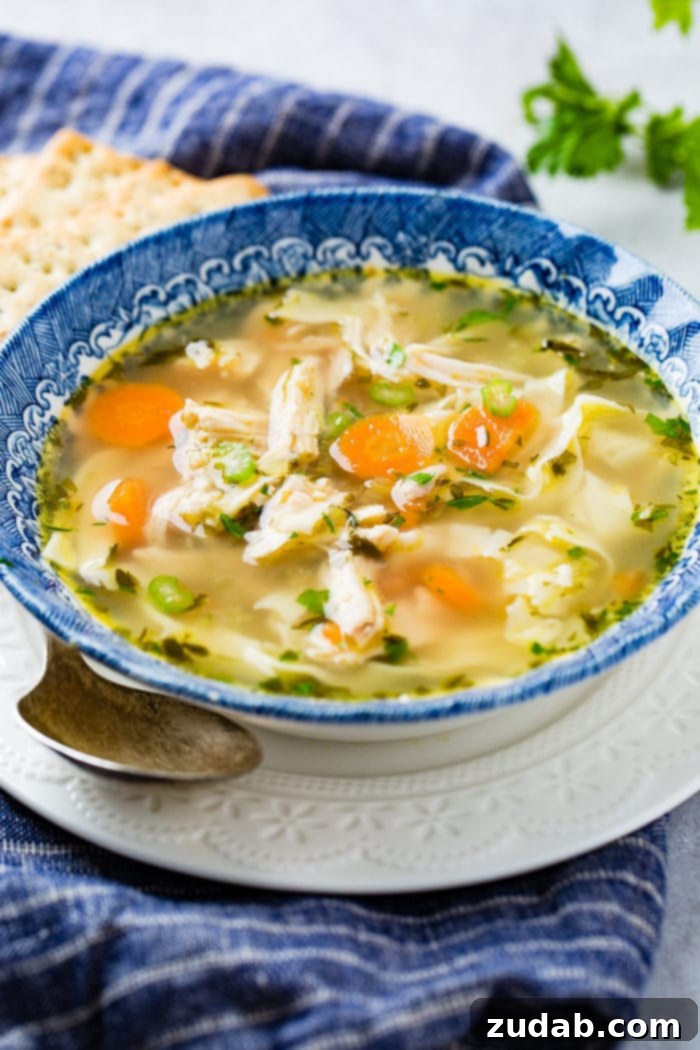 A inviting bowl of Instant Pot Chicken Noodle Soup in a rustic blue bowl, sitting on a white plate with a spoon, promising warmth and flavor.