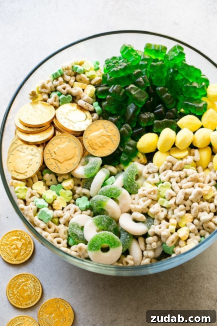 Lucky Leprechaun's 5-Minute Treat 2 A large glass bowl overflowing with a vibrant St. Patrick's Day snack mix, featuring golden chocolate coins, colorful Lucky Charms cereal, bright yellow lemon drops, chewy green apple gummy rings, and playful green gummy bears, all perfectly themed for the holiday.
