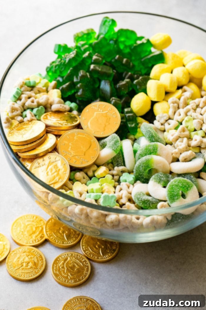 Lucky Leprechaun's 5-Minute Treat 4 A closer view of the large glass bowl filled with the delightful St. Patrick's Day snack mix, emphasizing the individual components: glistening chocolate gold coins, fluffy Lucky Charms marshmallows, translucent lemon drops, and chewy green apple gummy candies, all mixed for a perfect holiday treat.
