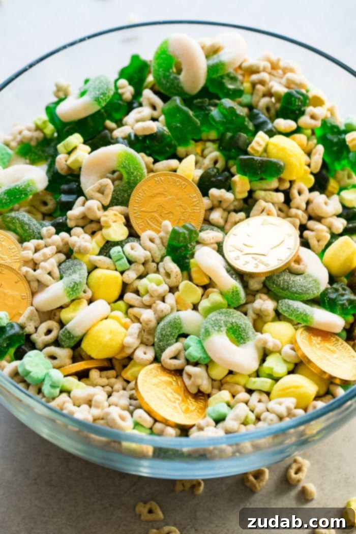 Lucky Leprechaun's 5-Minute Treat 6 A full, vibrant shot of the St. Patrick's Day snack mix, beautifully presented in a large glass bowl. All the festive ingredients – chocolate gold coins, Lucky Charms, lemon drops, green apple gummy rings, and green gummy bears – are perfectly blended, creating an inviting and irresistible treat for any celebration.